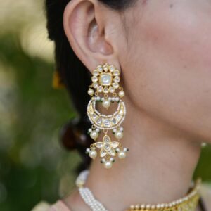 Close-up of a woman's ear adorned with luxurious gold earrings featuring pearls and gems.