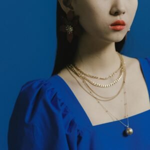 Portrait of a woman in a blue dress wearing gold necklaces, set against a blue background.