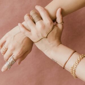 Elegant hands adorned with gold jewelry against a soft pink background, showcasing style and grace.